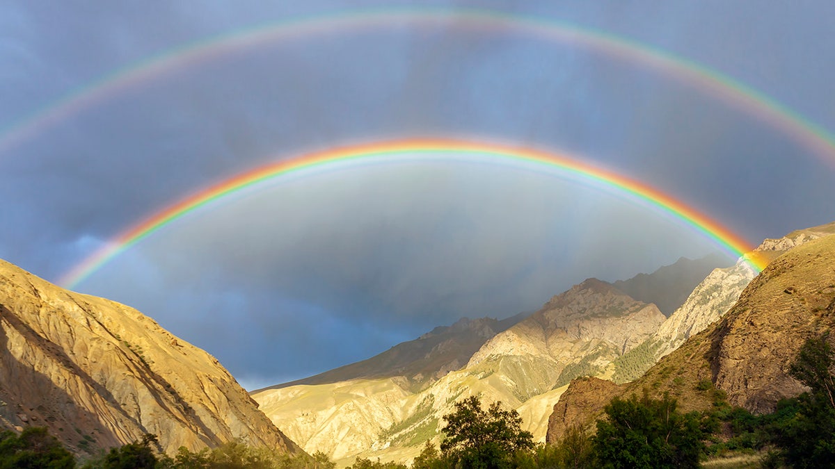 Rare double rainbow in the dark sky in the mountains.