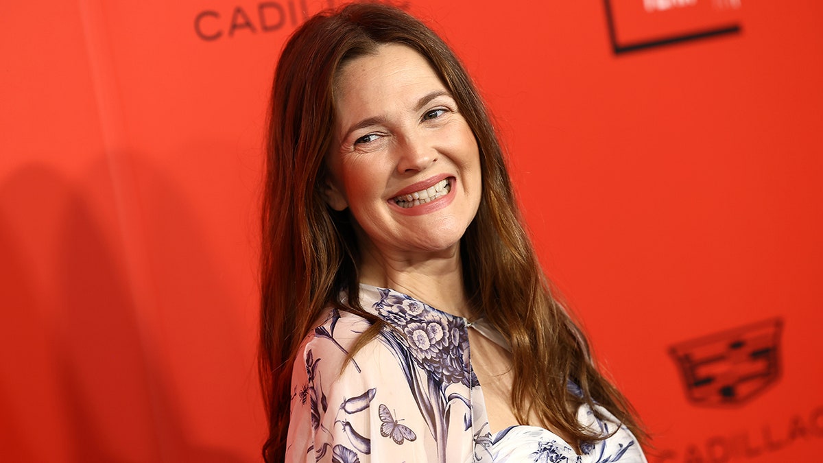 Drew Barrymore in a patterned silk dress smiles on the carpet in New York City and leans her head back slightly