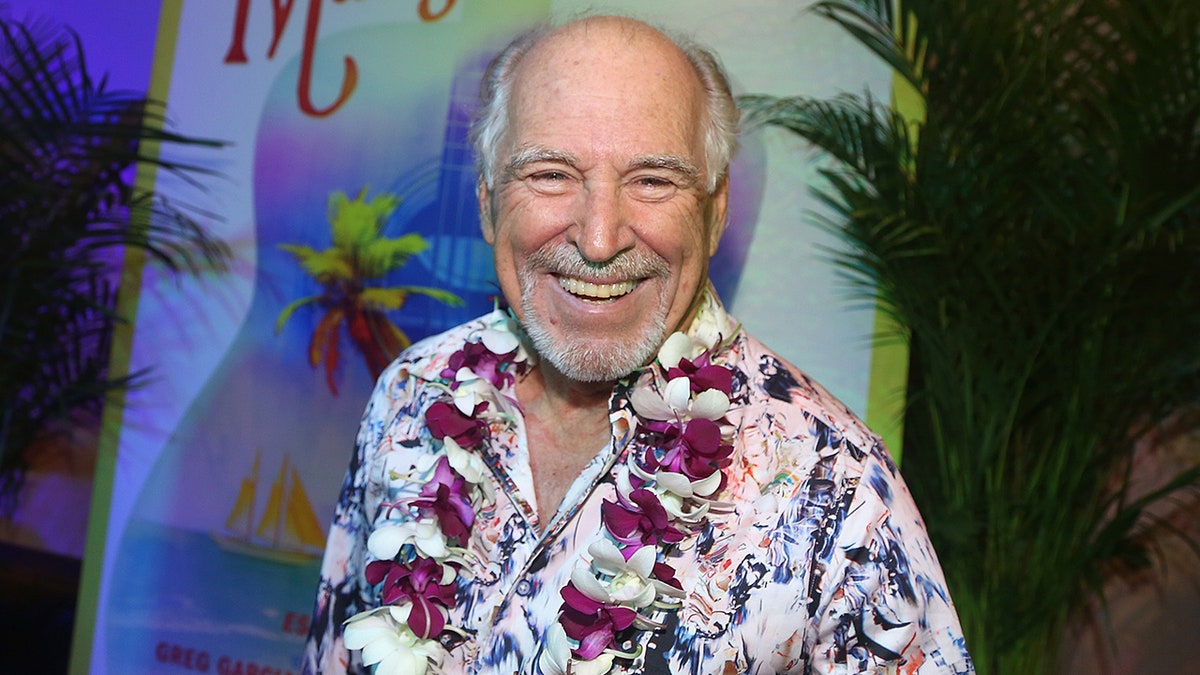 Jimmy Buffett smiles in a tropical shirt and a lei around his neck