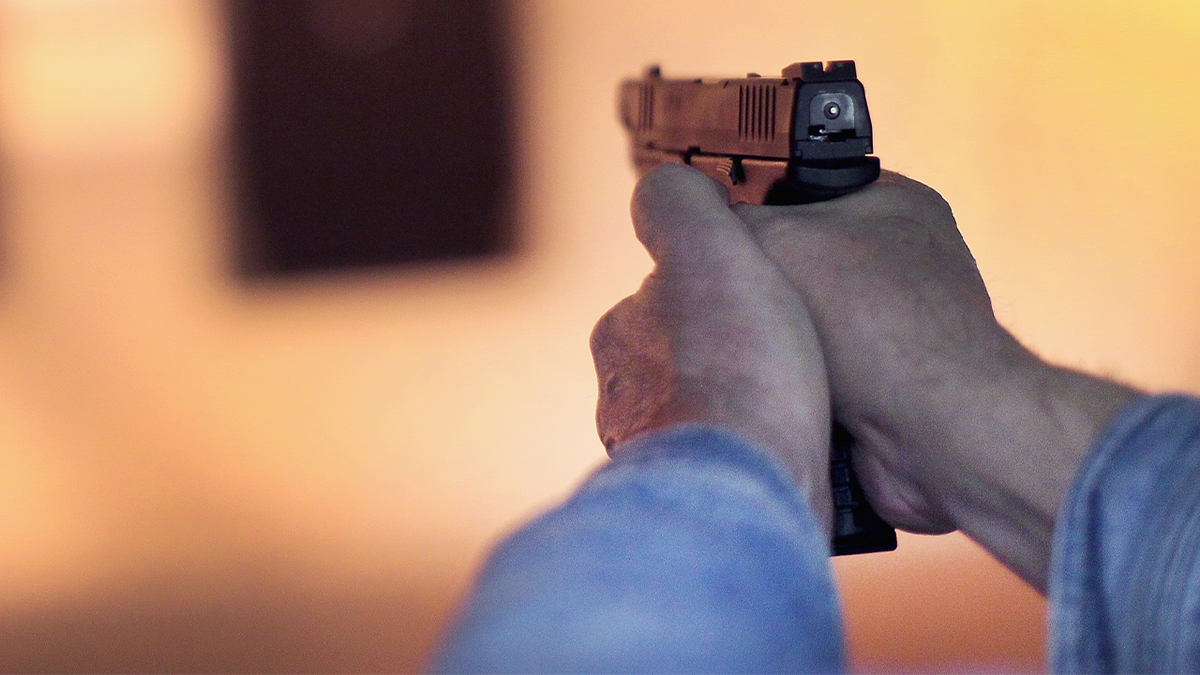 Man holding handgun, aiming at target at range
