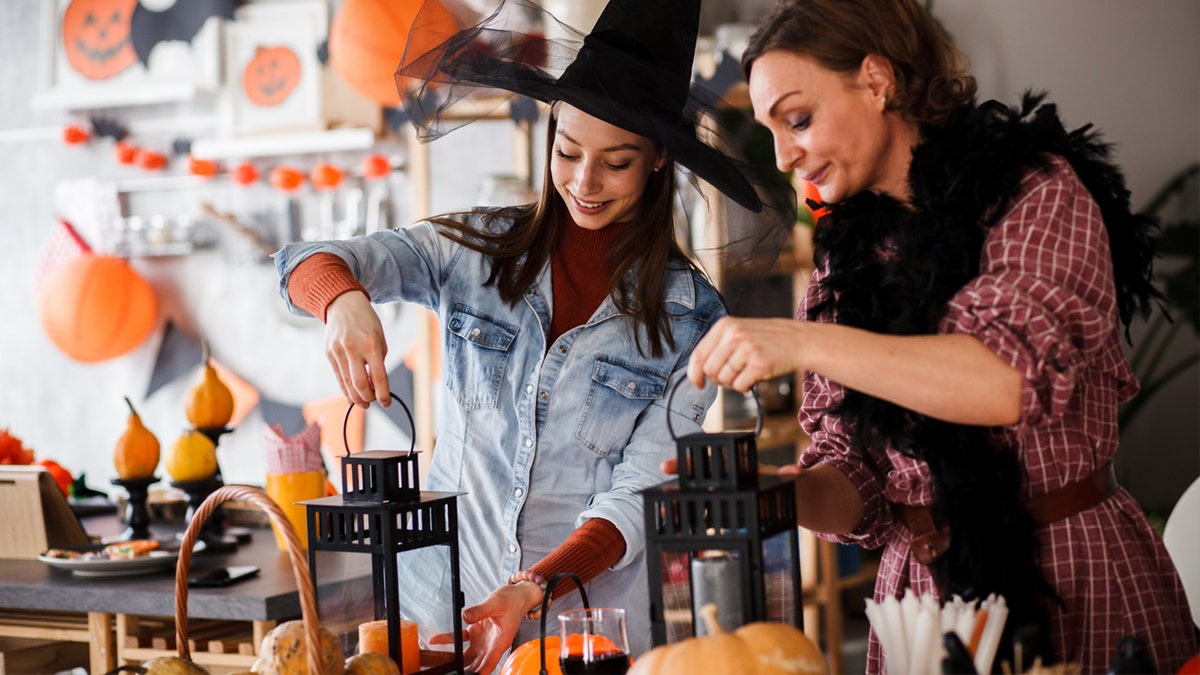 Two women light candles with Halloween decorations set up. 