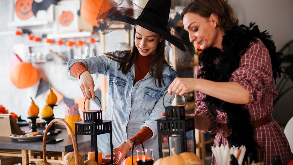 Two women light candles with Halloween decorations set up.