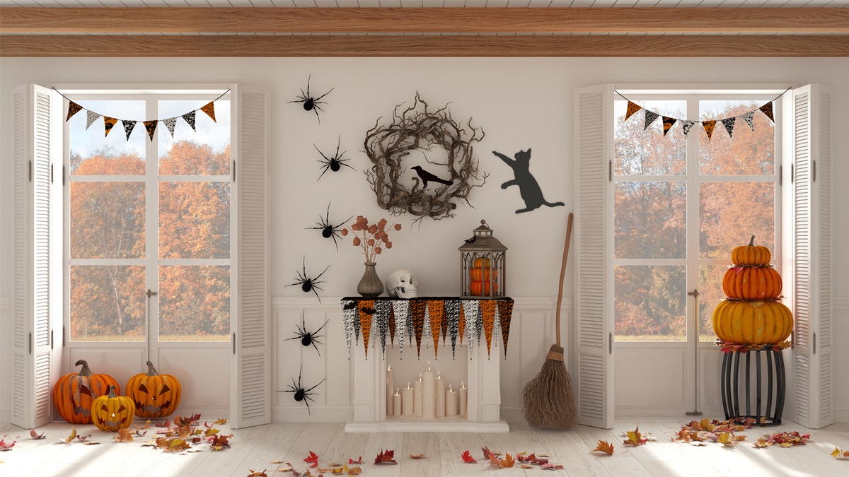 Home interior with Halloween decorations. The living room has a white fireplace and panoramic windows with autumn views.