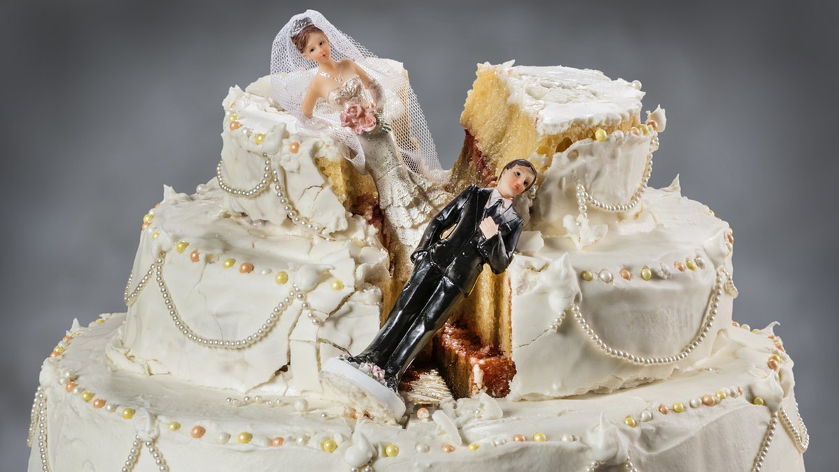 A smashed three-tier wedding cake with fallen bride and groom cake toppers.