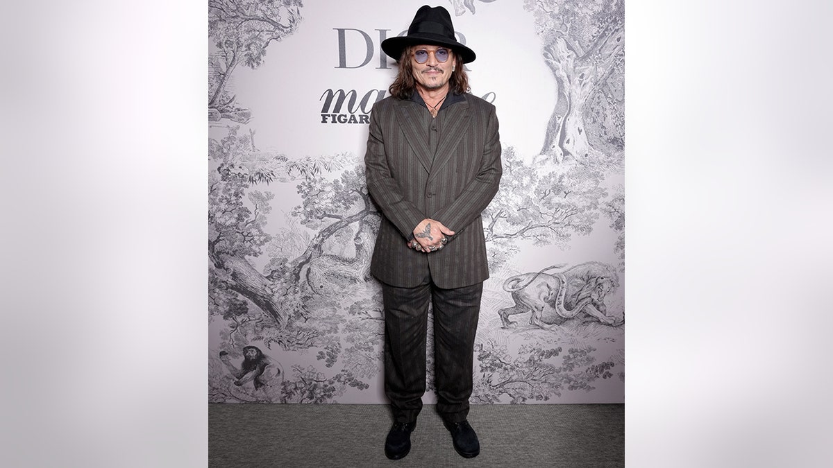 Johnny Depp in a grey striped suit and pants and a hat at an event with Dior