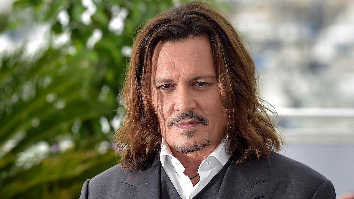 Johnny Depp in a grey suit and undervest stares at the camera on the carpet in Cannes