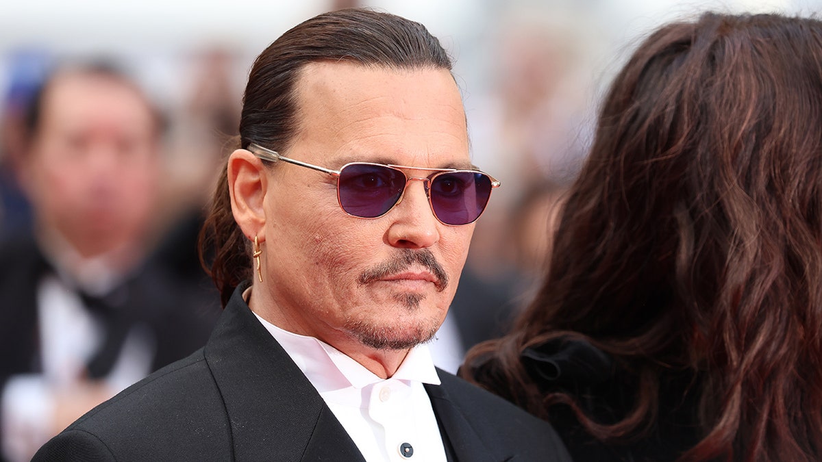 Johnny Depp wearing sunglasses on the Cannes carpet with his hair slicked back and in a black suit