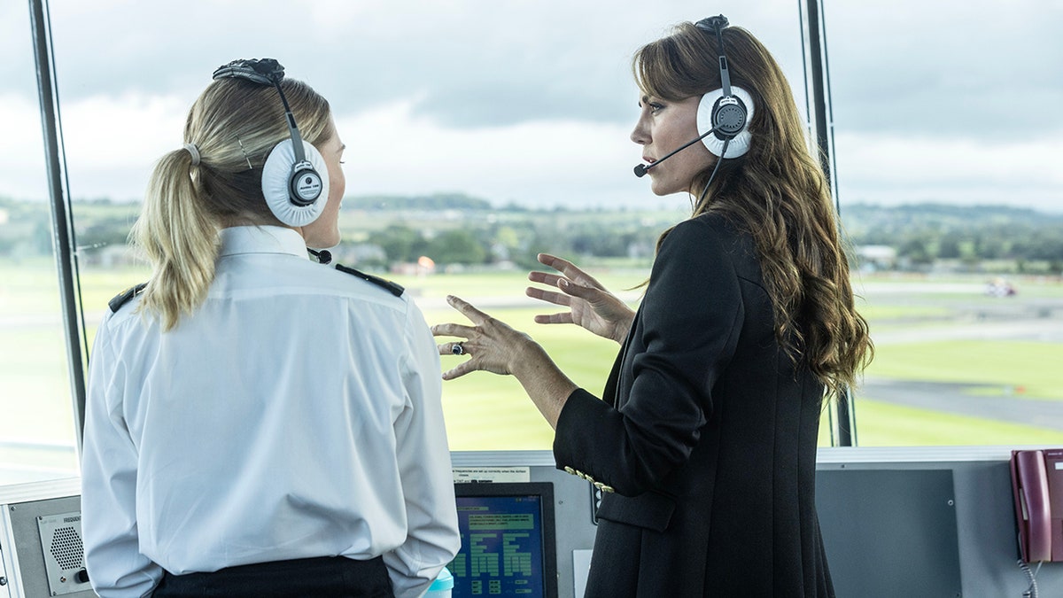 Kate Middleton talks with her hands as she wears headphones and speaks with a member of the Royal Navy wildcat helicopter