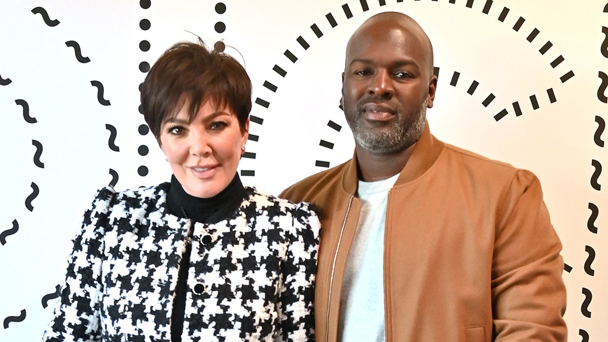 Corey Gamble in a houndstooth jacket poses with Corey Gamble in a brown leather jacket on the carpet