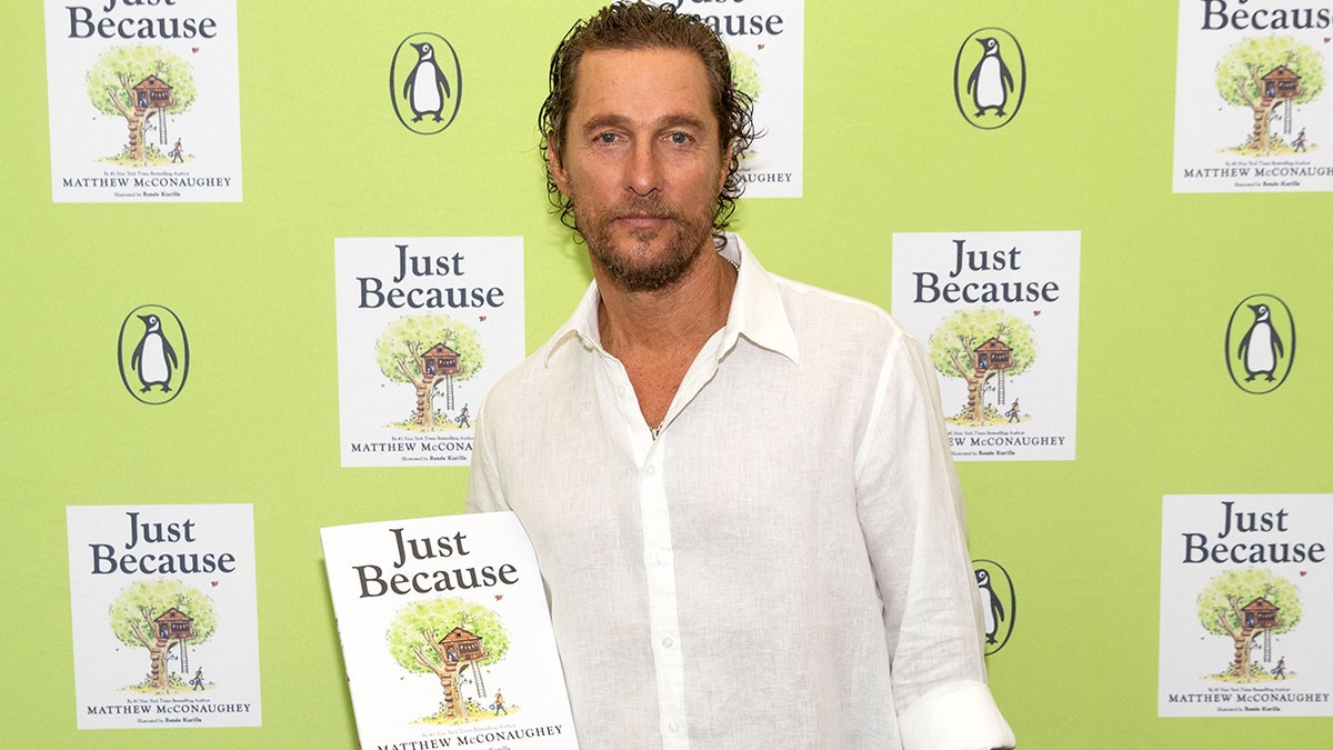 Matthew McConaughey in a white button down shirt holds his book "Just Because" on a carpet in Austin, Texas