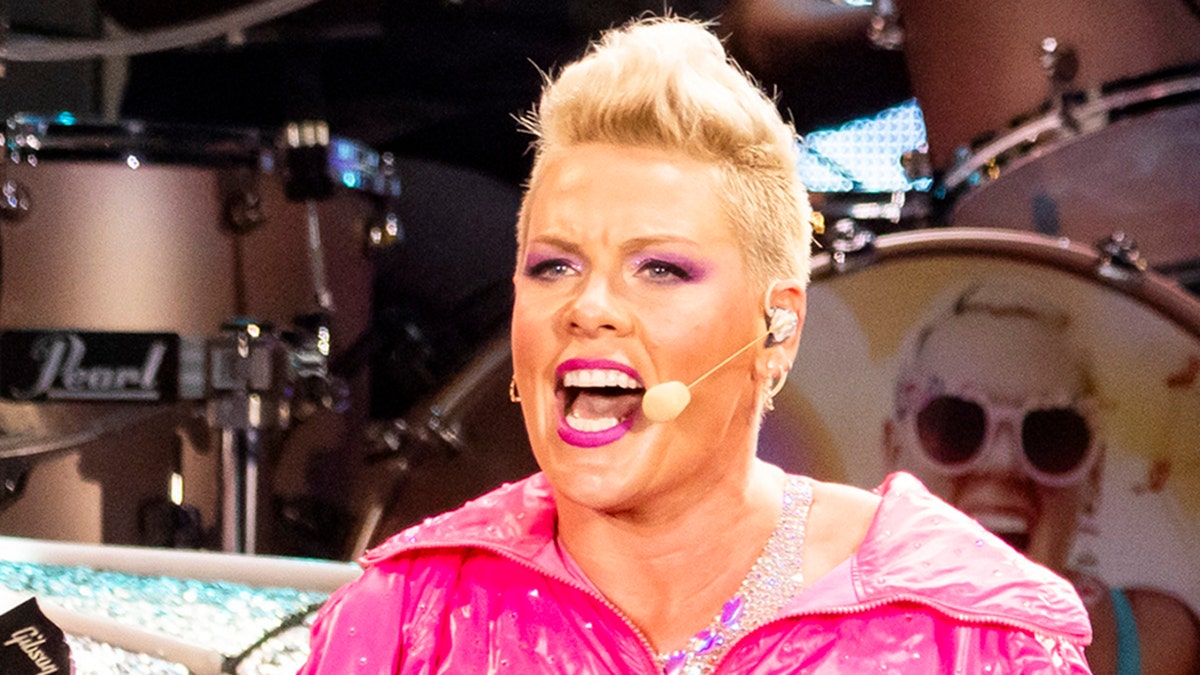 Pink performing on stage looks passionate as she sings into her headset microphone in a hot pink jacket