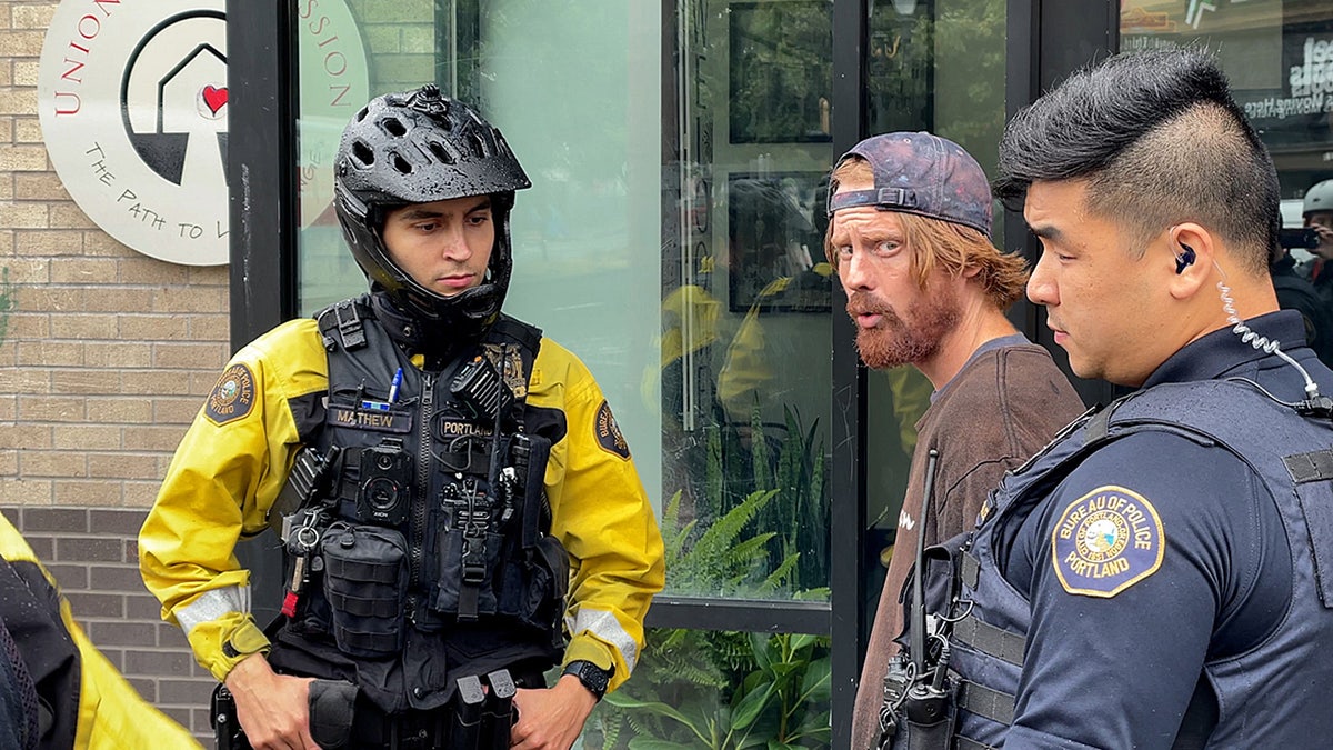 Portland bike squad officer stands next to suspect being arrested