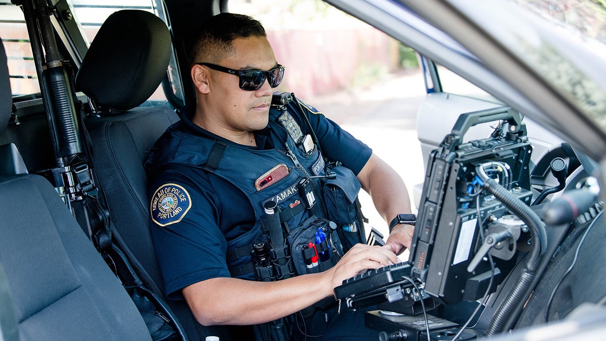 A Portland police officer sits inside his patrol car, typing