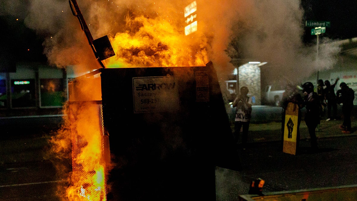 Flames spill from a dumpster at night in Portland, Oregon