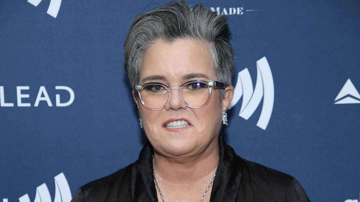 Rosie O'Donnell smiles in a dark jacket and glasses