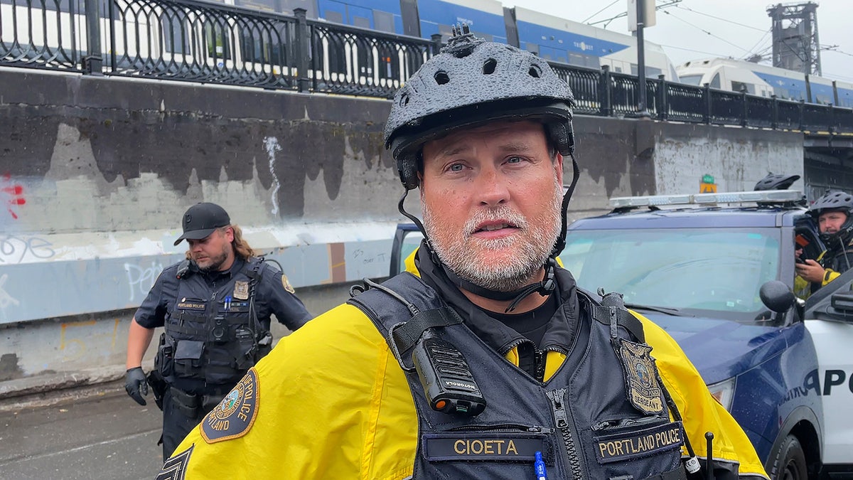 Portland bike squad sergeant stands with police car and MAX train