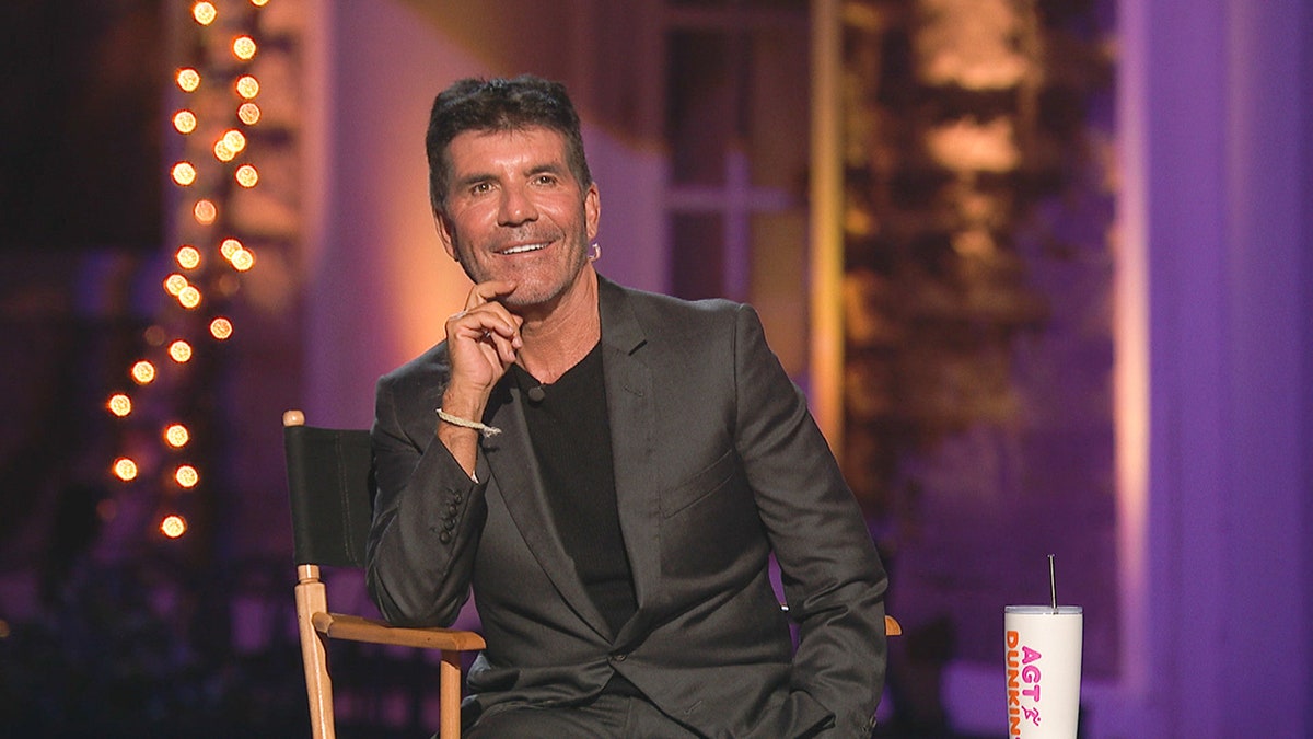 Simon Cowell puts his hand to his chin as he watches a performance in a chair