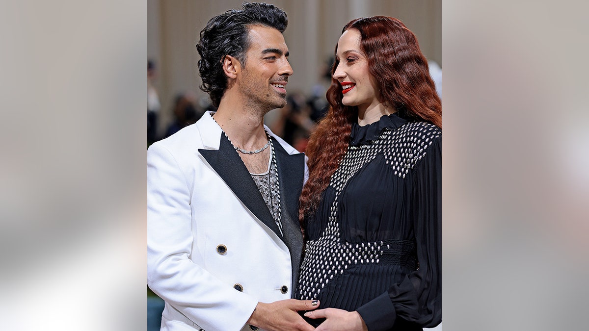 Joe Jonas in a white suit cradles Sophie Turner's baby bump at the Met Gala