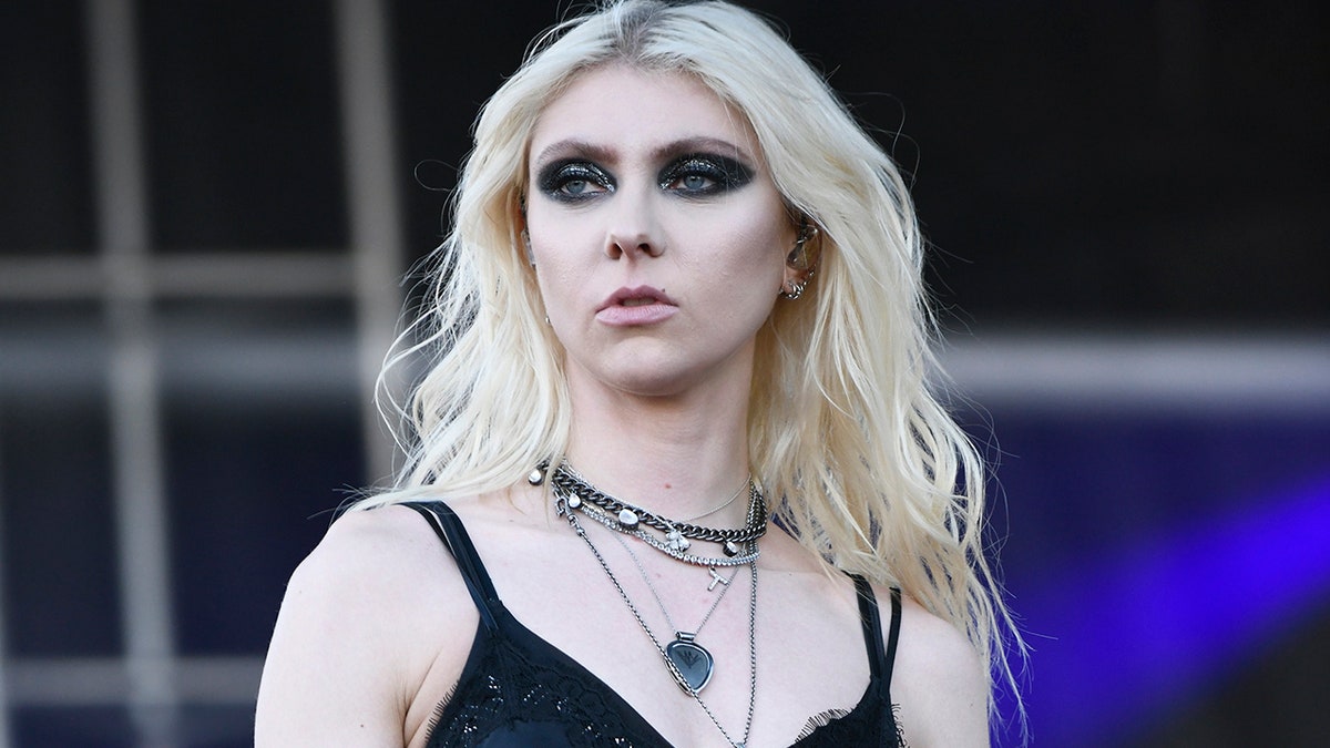 Taylor Momsen with dark black eyeshadow in a black top and jewelry on stage