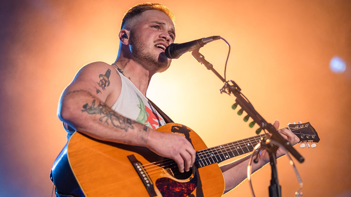 Zach Bryan playing guitar on stage