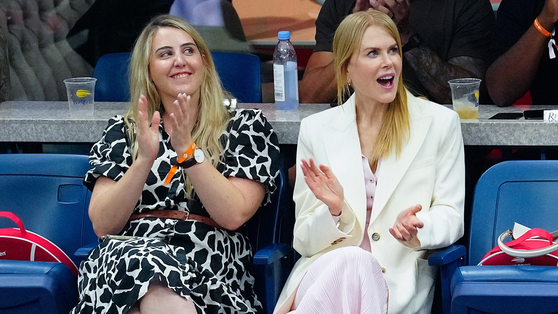 Nicole Kidman in a pink dress and white blazer claps while watching the US Open