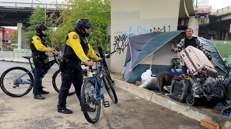Two bicycle officers stand near tents in Portland homeless camp