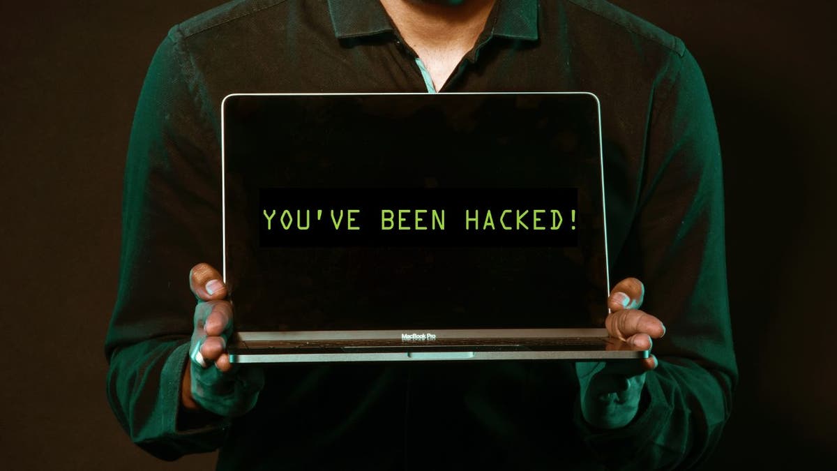 Pessoa segurando um laptop com as palavras "Você foi hackeado!" na tela.