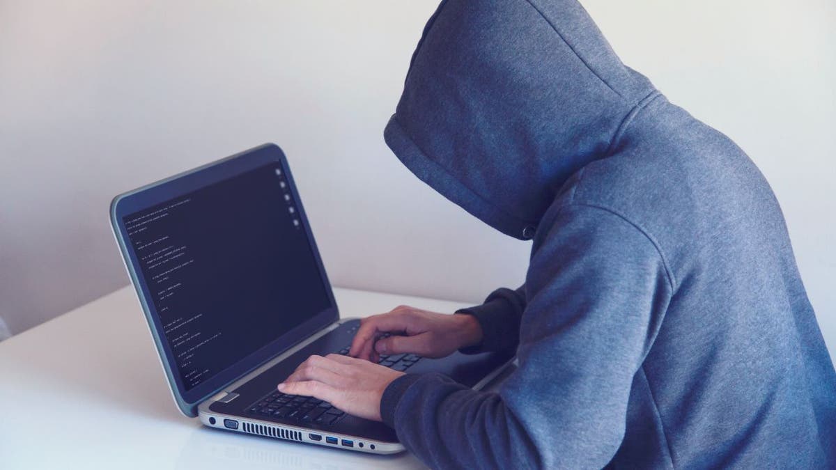Hooded hacker typing on his laptop.