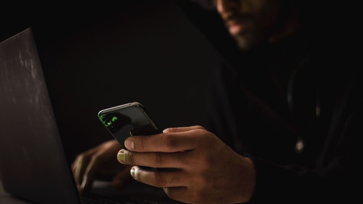 Photo of a person using their laptop while holding their phone.