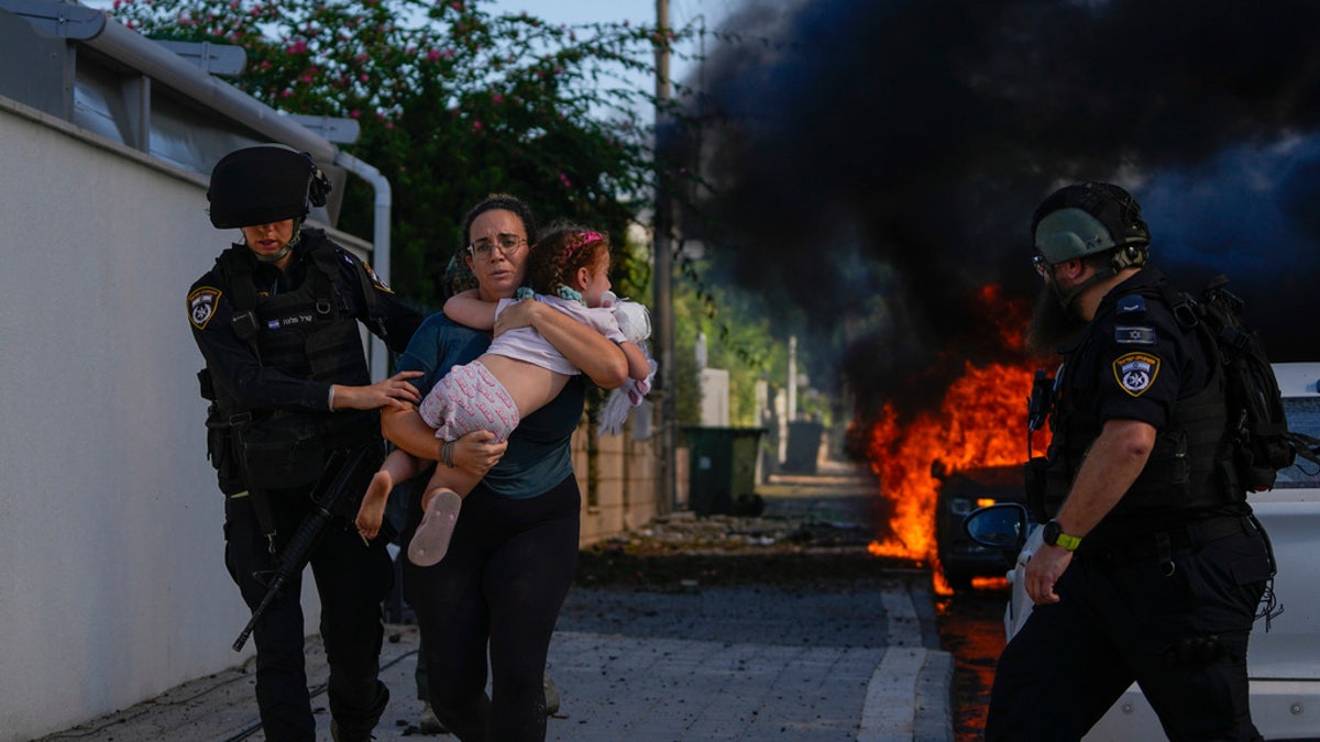Police officers evacuate a woman and a child from a site hit by a rocket fired from the Gaza Strip, in Ashkelon, southern Israel, Saturday, Oct. 7, 2023. (AP Photo/Tsafrir Abayov)