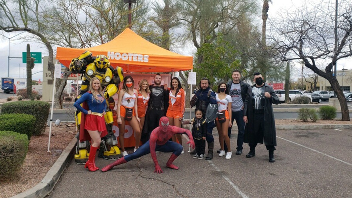 Averey Tressler smiling alongside other Hooters girls and people in superhero costumes