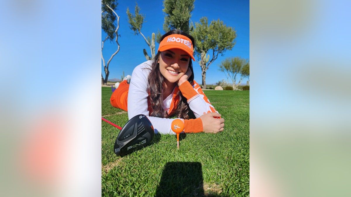 Averey Tressler wearing a Hooters golf uniform while laying on grass