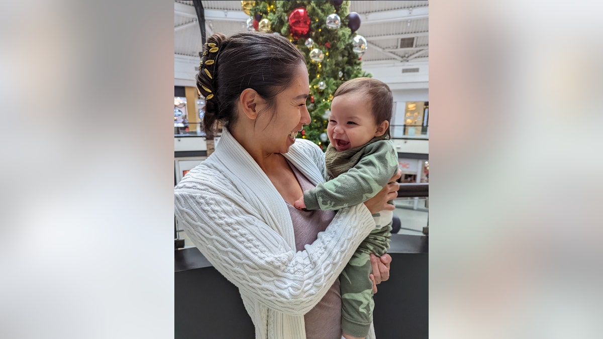 Brittney Mesa hugs her infant son, Greyson, in front of a Christmas tree.