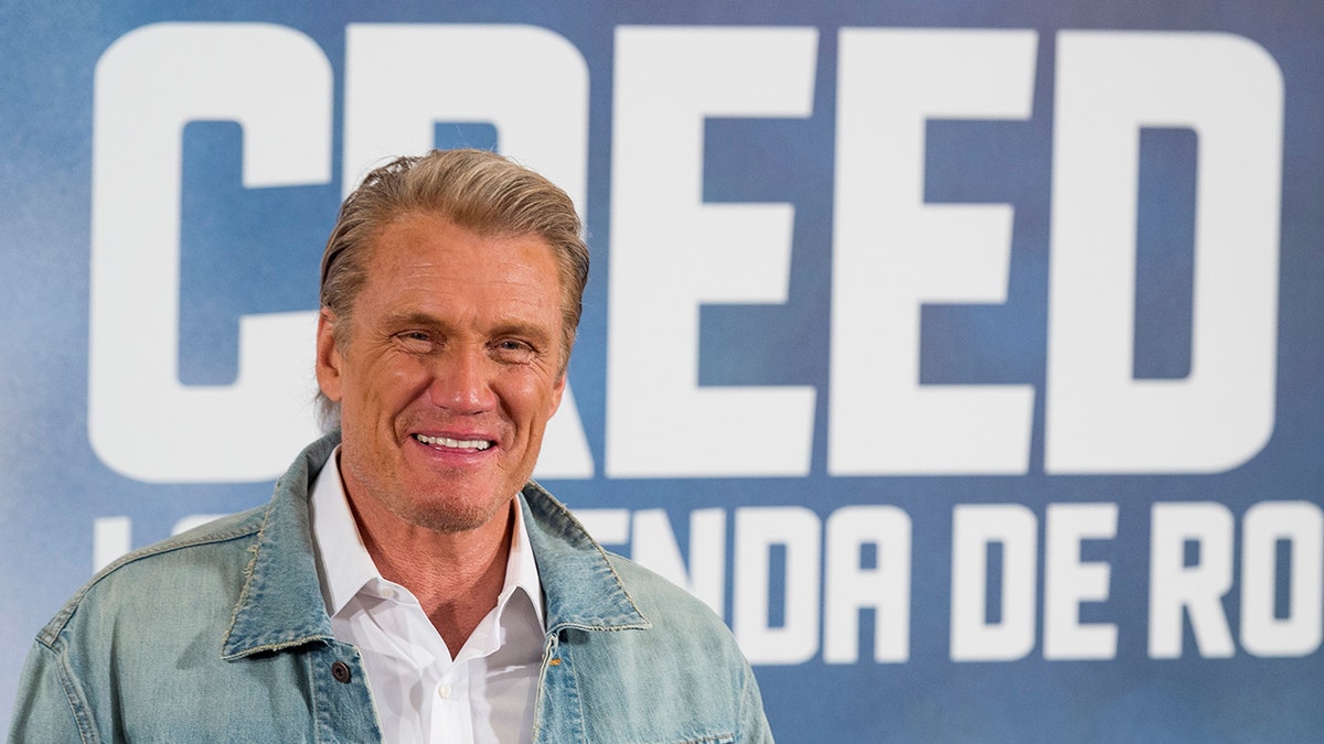 Dolph Lundgren posing in front of Creed signage