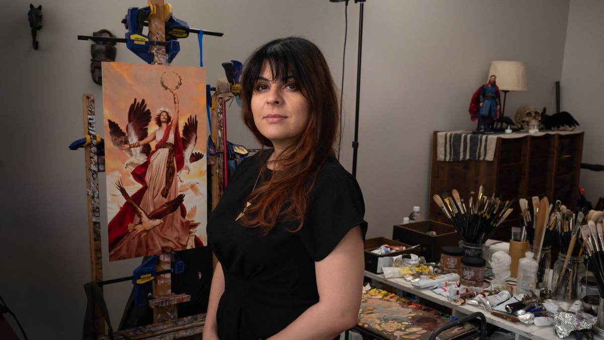 Karla Ortiz poses in her art studio with a painting behind her