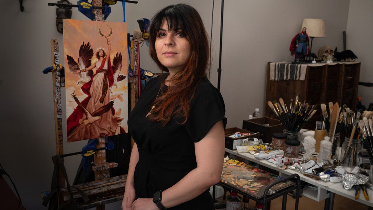 Karla Ortiz poses in her art studio with a painting behind her