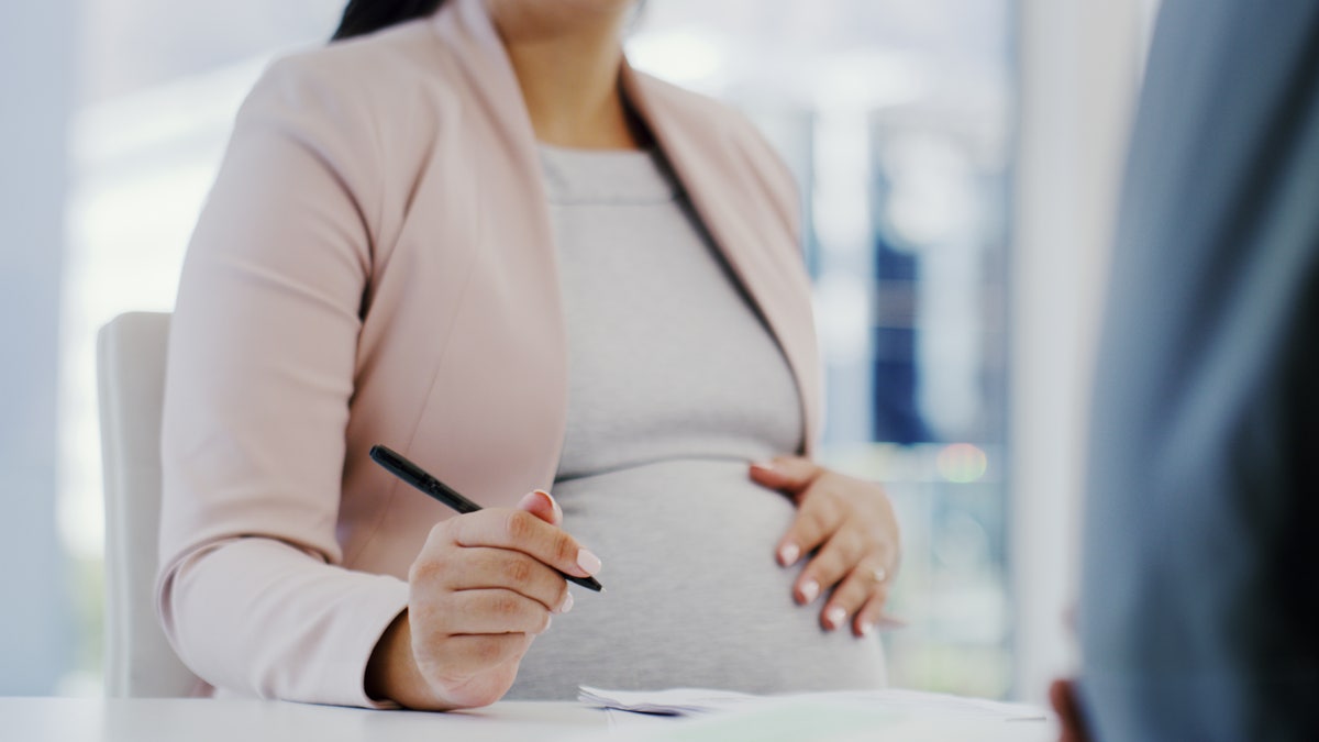Cropped shot of a woman touching her pregnant belly while sitting in a meeting
