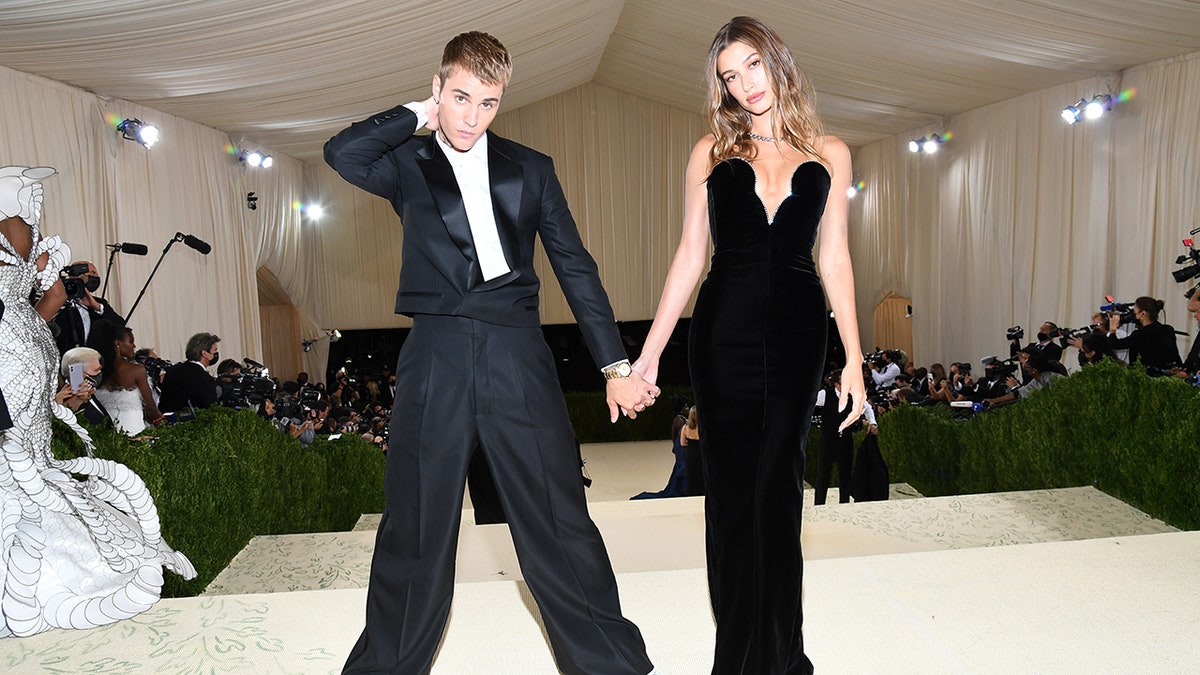 Justin Bieber in a black suit holds hands with Hailey Bieber in a black plunging gown at the Met Gala