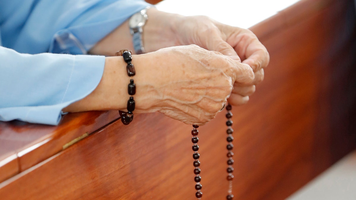 La mano de una mujer sostiene un rosario.