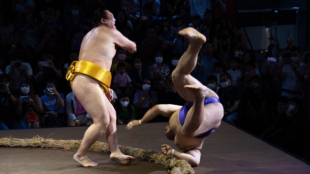 sumo wrestler knocks another wrestler out of the ring
