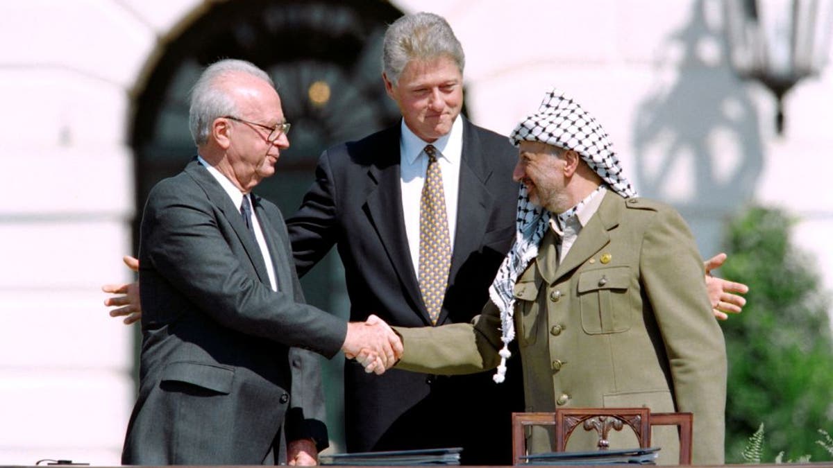 President Bill Clinton stands behind Yassar Arafat and Israeli Prime Minister Yitzhak Rabin