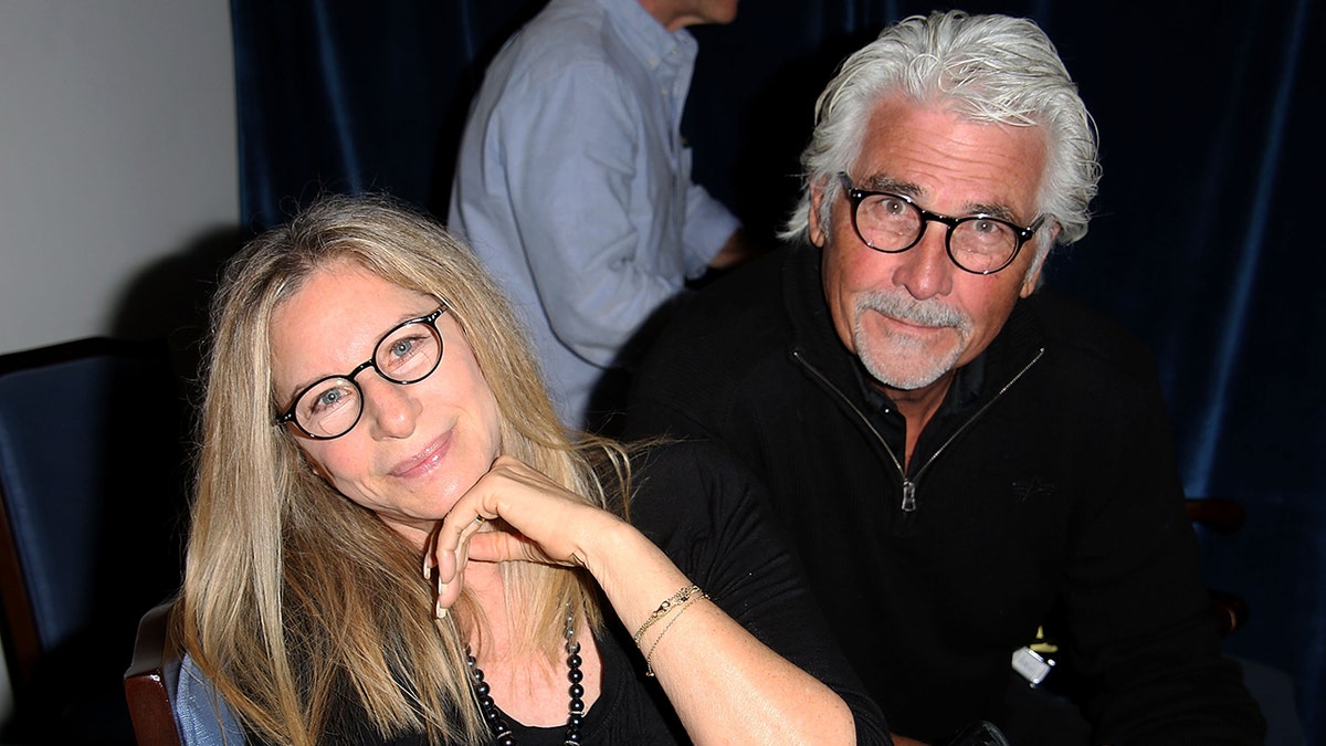 Barbra Streisand and James Brolin wearing matching black outfits and reading glasses