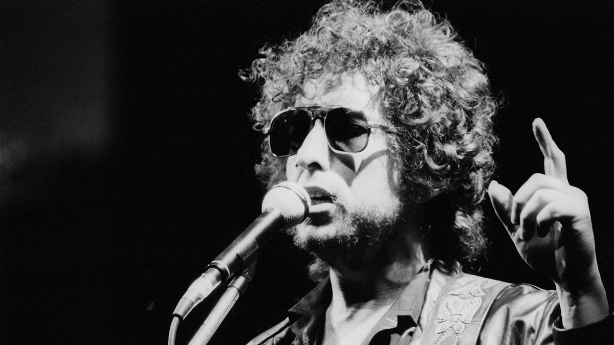 Um close de Bob Dylan apontando para cima enquanto canta