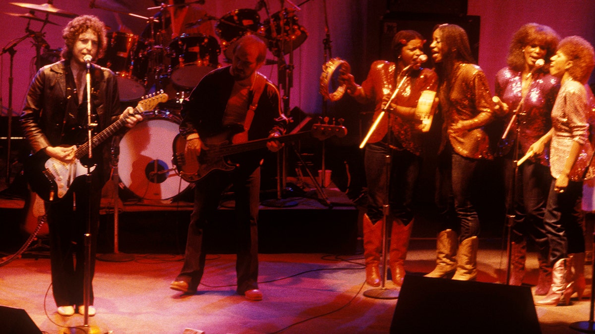 Bob Dylan performing live on stage with a group of musicians