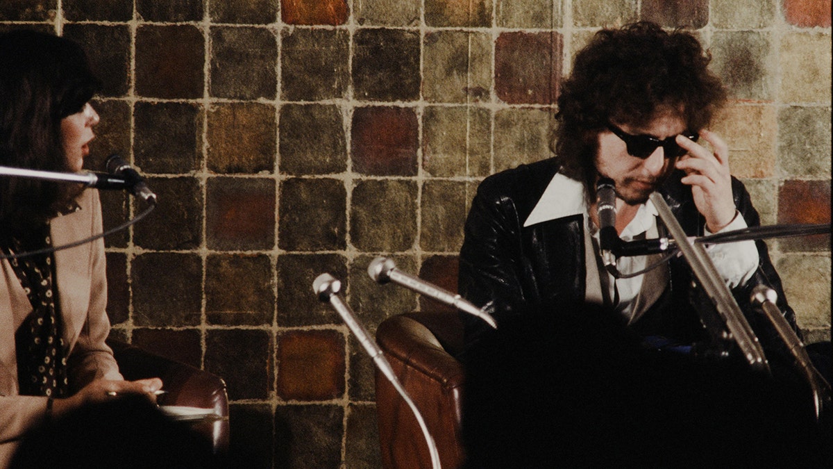 Bob Dylan looking downcast as a Japanese reporter looks on