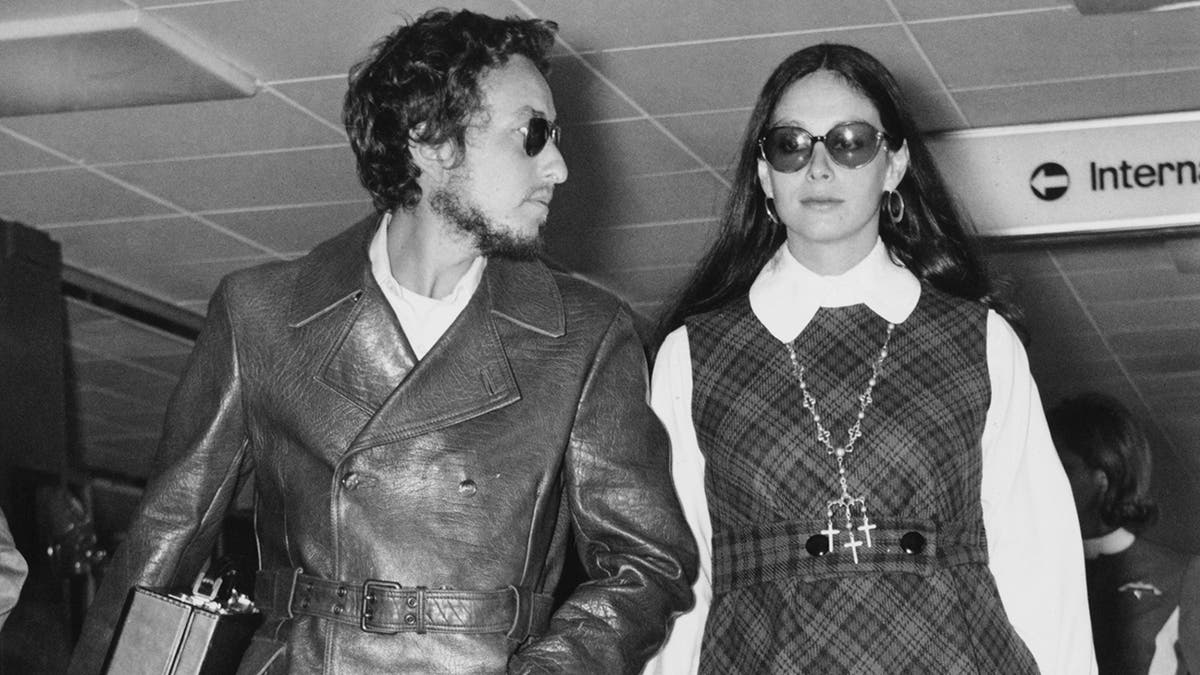 Bob Dylan olhando para sua esposa Sara no aeroporto enquanto os dois usam óculos escuros