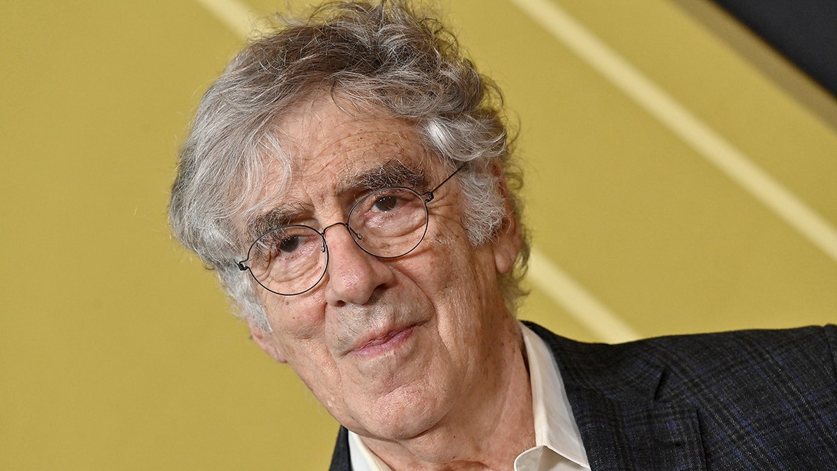 A close-up of Elliott Gould in a suit with reading glasses
