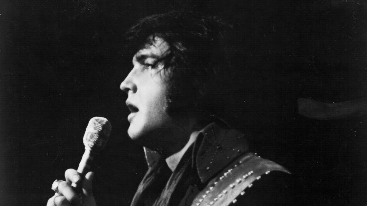A black side profile of Elvis Presley singing on stage