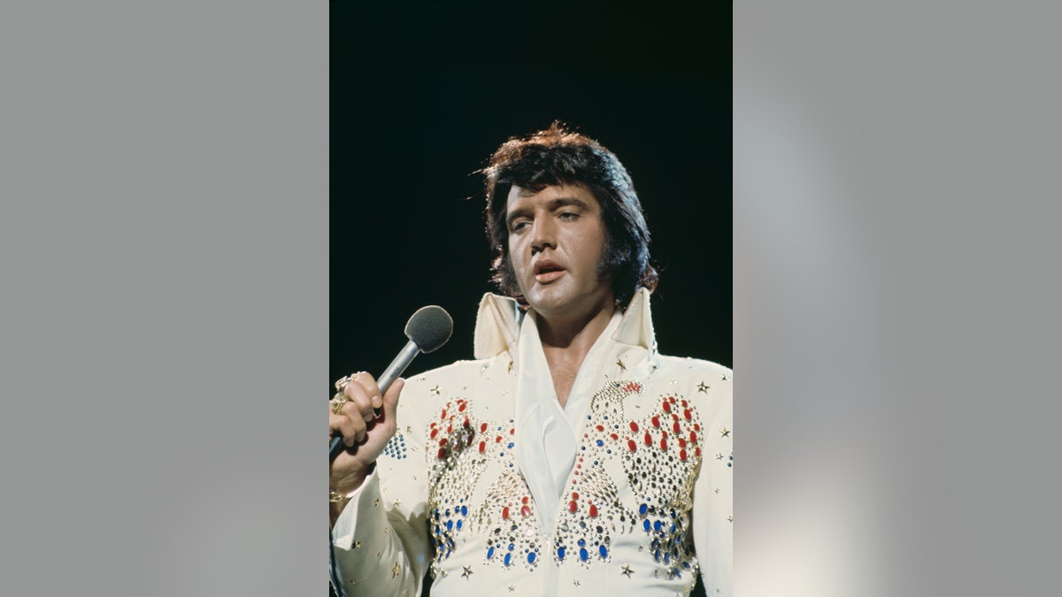 Elvis Presley wearing a studded white jumpsuit and holding a mic