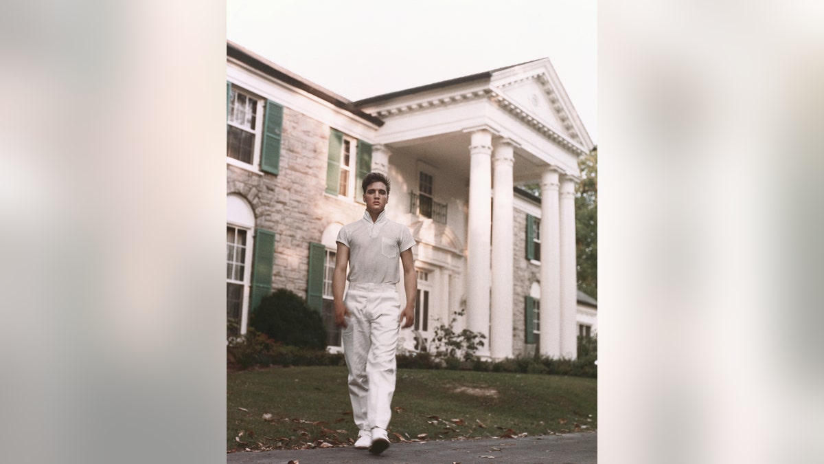 Elvis Presley dressed in all white standing in front of Graceland
